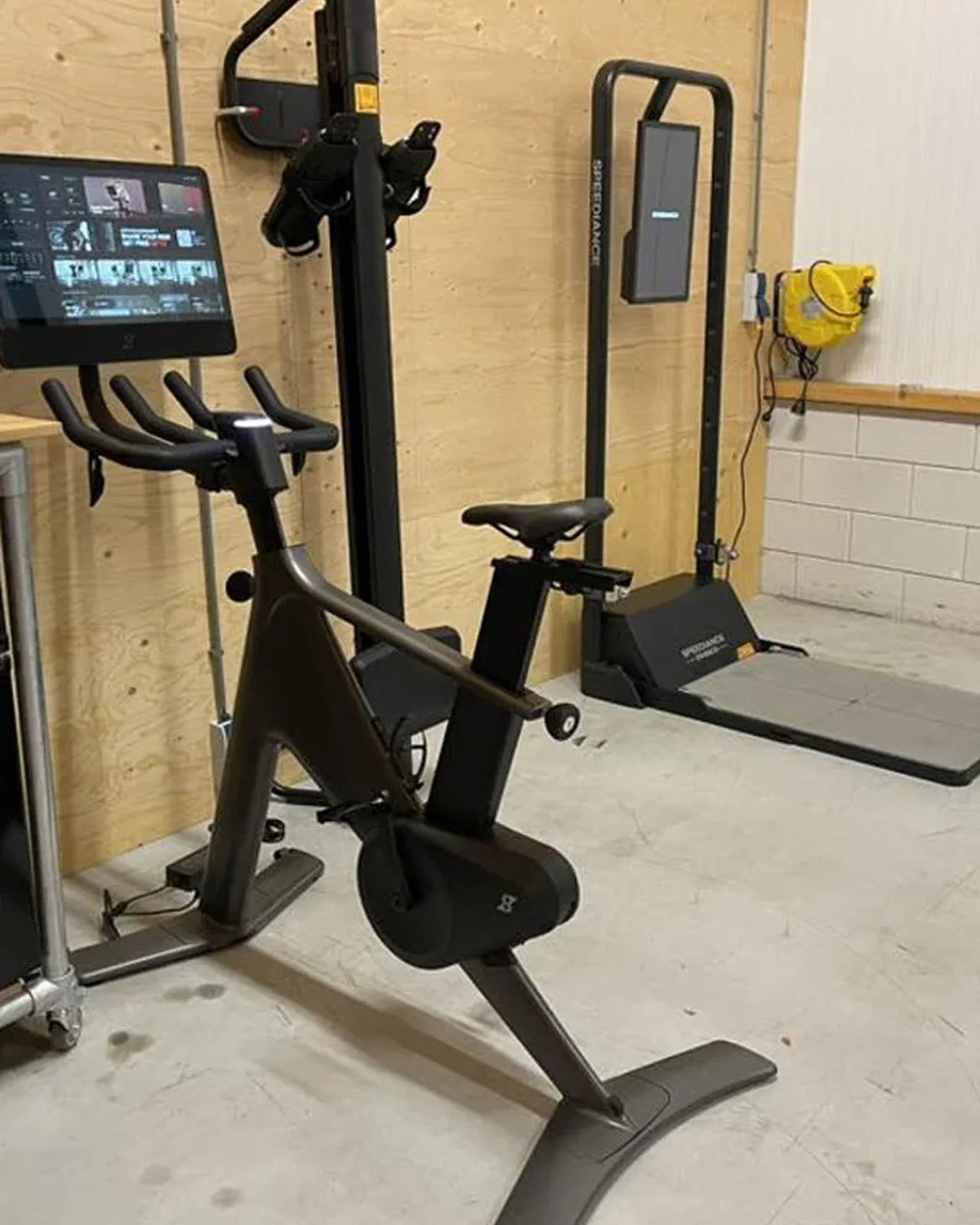Exercise bike in a home gym setting with wooden walls and a tiled floor.