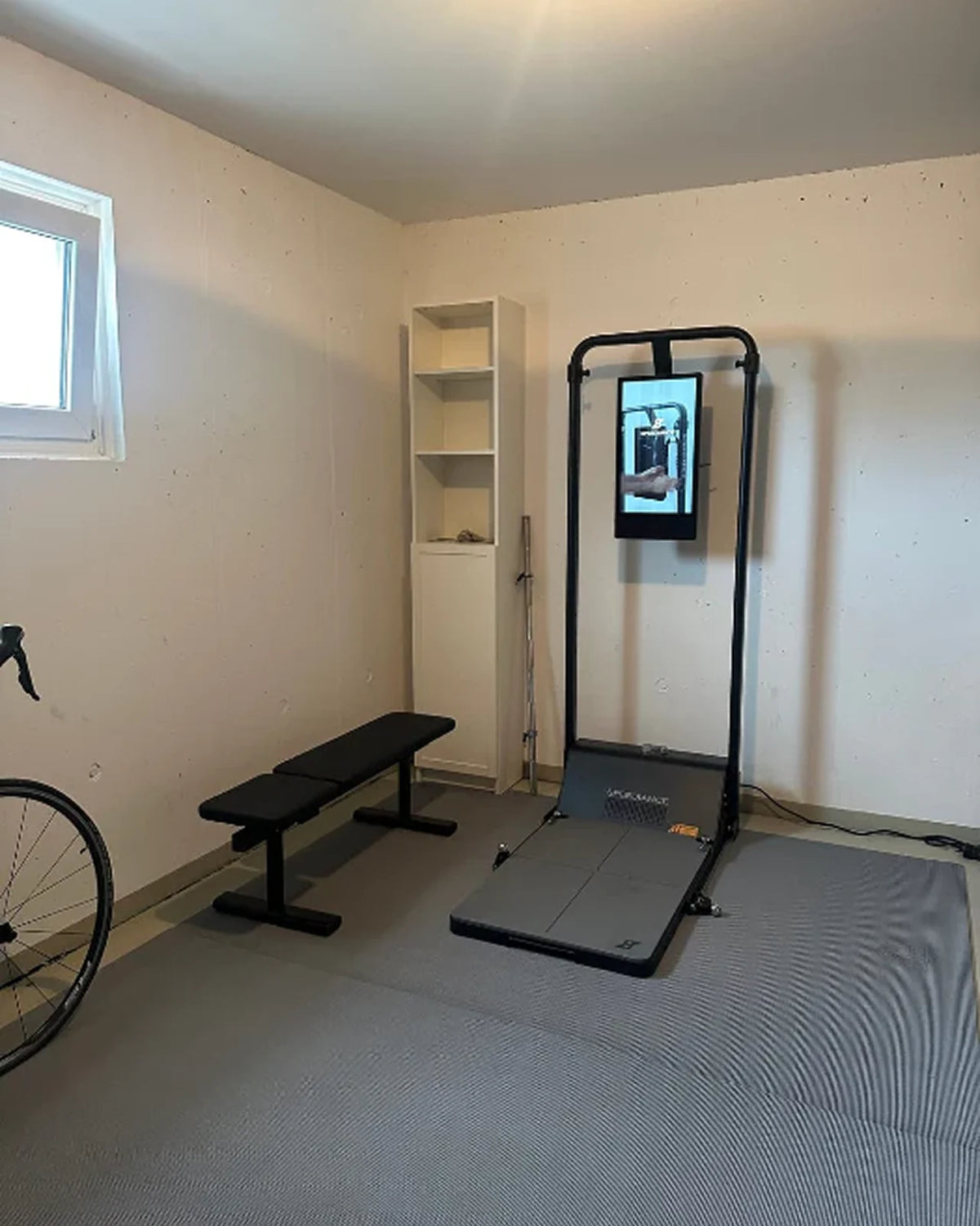 Home gym setup with bench, treadmill, and screen in a room.