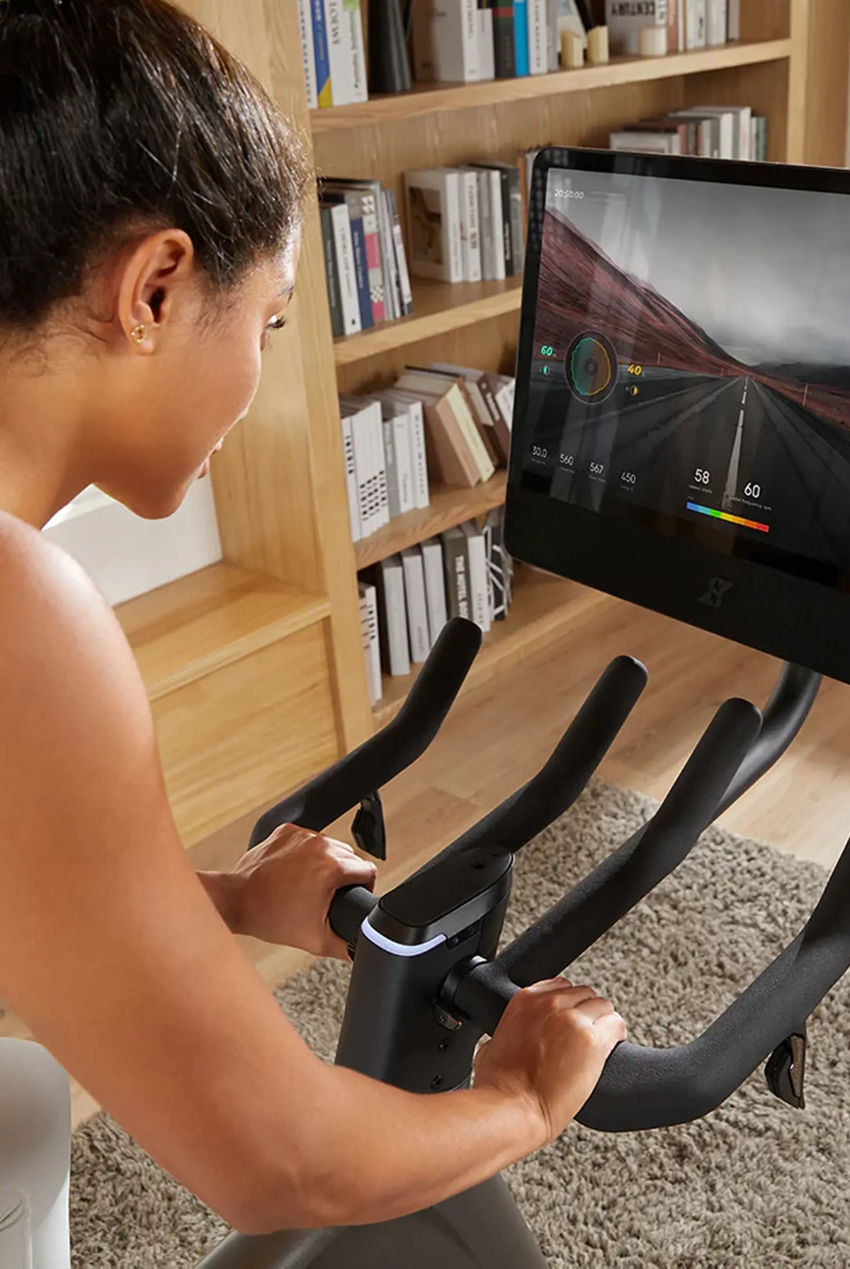 Person using a stationary bike with a tablet displaying a cycling app in a home setting.