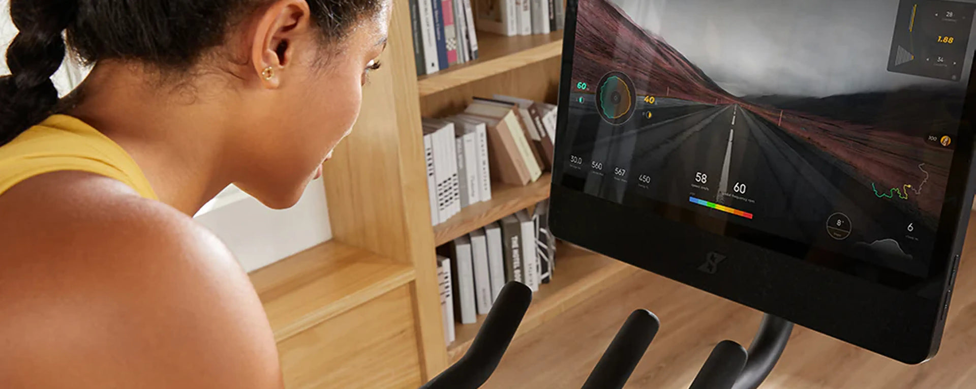 Person using a fitness monitor on an exercise bike with a bookshelf in the background